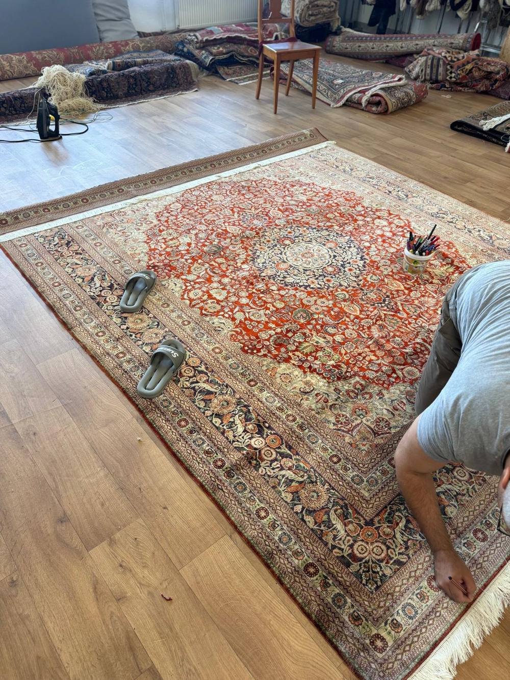 Contrôle d’un grand tapis de soie étalé à plat avant la restitution.